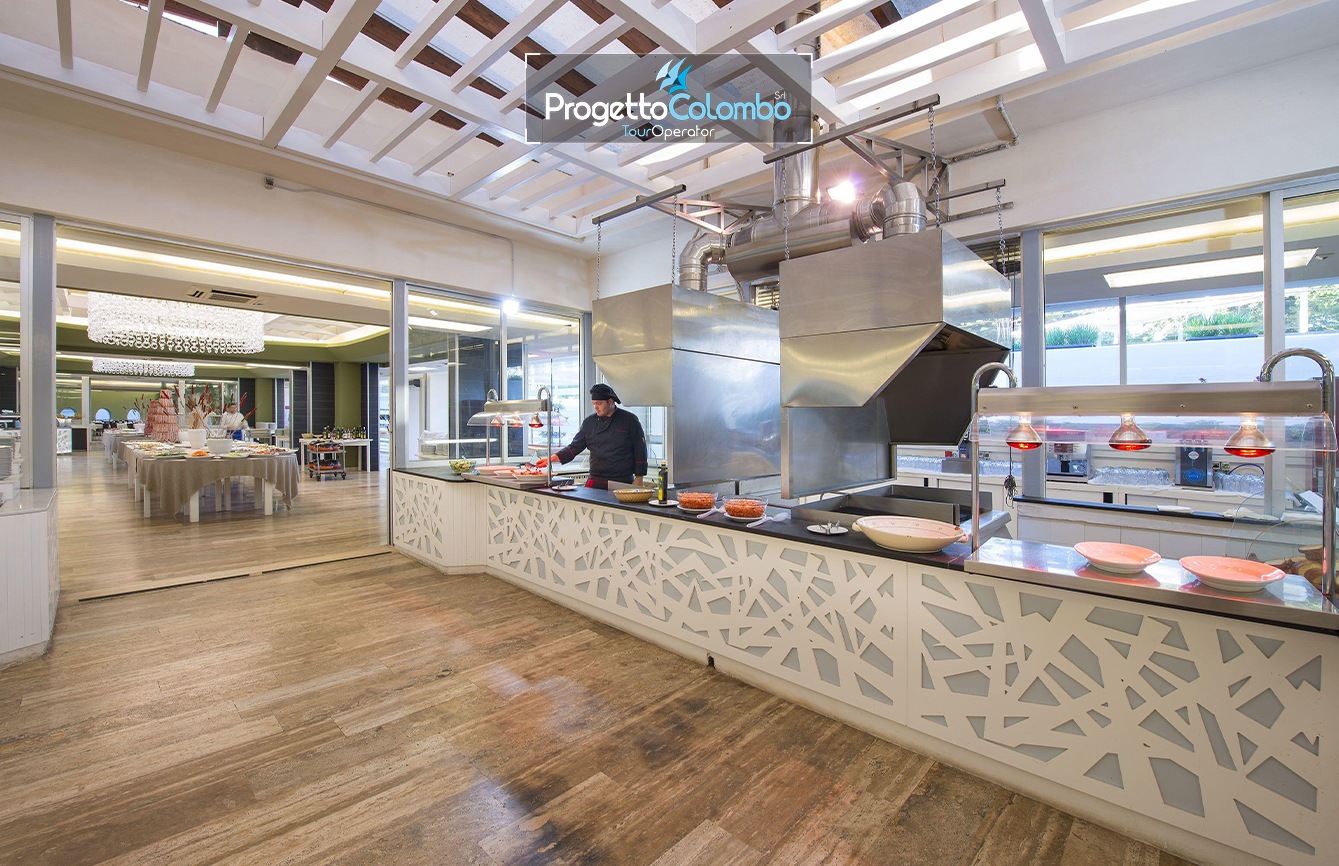 Progetto Colombo Bari, Tour Operator, Mare Italia, Voi Alimini resort, Alpitour, Bravo Club, All Inclusive, Top Club, Puglia, Salento_Buffet 3 Spiaggia e Mare: "Spiaggia di sabbia bianca e mare cristallino del VOI Alimini Resort a Otranto, ideale per vacanze a metà settembre." Piscina: "Ampia piscina all'aperto circondata dal verde del giardino nel resort VOI Alimini in Puglia." Ristorazione: "Buffet vario e colorato nella sala ristorante del VOI Alimini Resort per gli ospiti in formula all-inclusive." Organizzazione Progetto Colombo Viaggi Bari