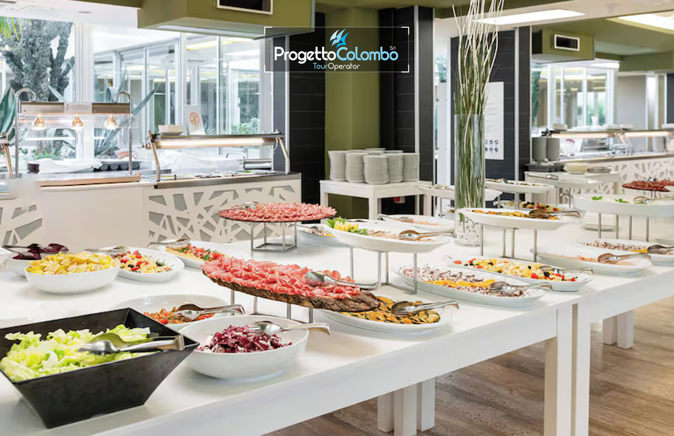 Progetto Colombo Bari, Tour Operator, Mare Italia, Voi Alimini resort, Alpitour, Bravo Club, All Inclusive, Top Club, Puglia, Salento_Buffet 4 Spiaggia e Mare: "Spiaggia di sabbia bianca e mare cristallino del VOI Alimini Resort a Otranto, ideale per vacanze a metà settembre." Piscina: "Ampia piscina all'aperto circondata dal verde del giardino nel resort VOI Alimini in Puglia." Ristorazione: "Buffet vario e colorato nella sala ristorante del VOI Alimini Resort per gli ospiti in formula all-inclusive." Organizzazione Progetto Colombo Viaggi Bari