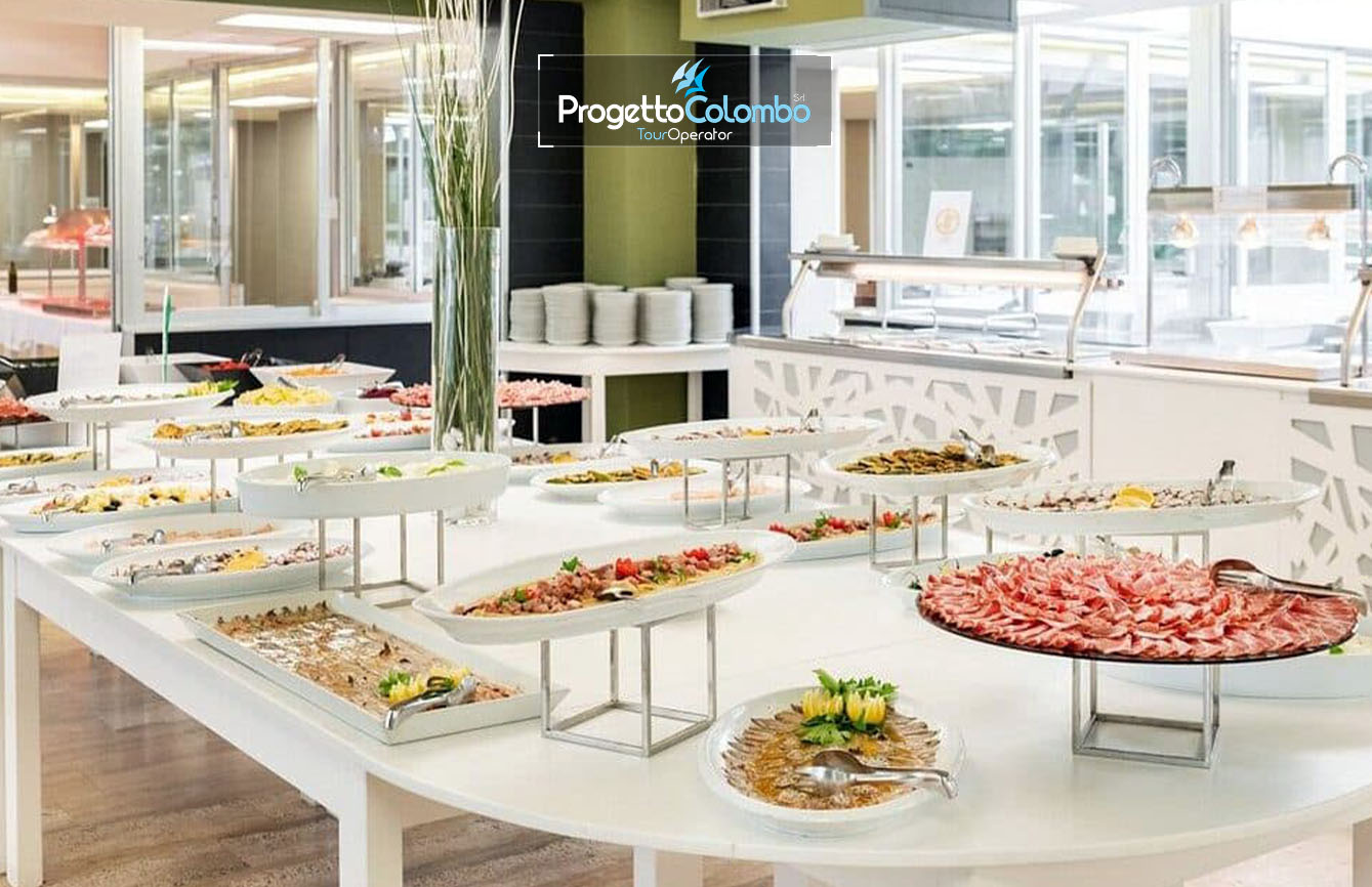 Progetto Colombo Bari, Tour Operator, Mare Italia, Voi Alimini resort, Alpitour, Bravo Club, All Inclusive, Top Club, Puglia, Salento_Buffet Spiaggia e Mare: "Spiaggia di sabbia bianca e mare cristallino del VOI Alimini Resort a Otranto, ideale per vacanze a metà settembre." Piscina: "Ampia piscina all'aperto circondata dal verde del giardino nel resort VOI Alimini in Puglia." Ristorazione: "Buffet vario e colorato nella sala ristorante del VOI Alimini Resort per gli ospiti in formula all-inclusive." Organizzazione Progetto Colombo Viaggi Bari